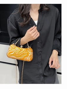 Detail of evening bag with orange and gold wave patterns and metallic chain handle