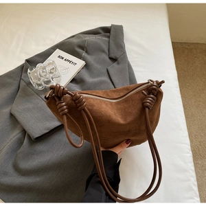 Close-up of brown suede crescent bag with leather knot strap on a grey blazer