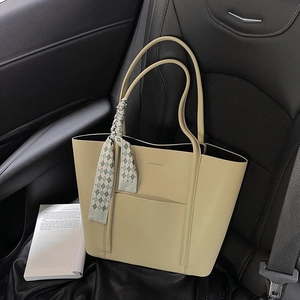 Detail of light khaki lychee grain tote bag with decorative scarf on car leather seat