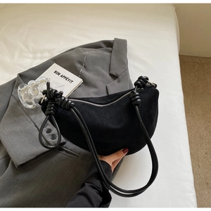Detail of black crescent shoulder bag with knotted strap and silver zipper on a grey blazer