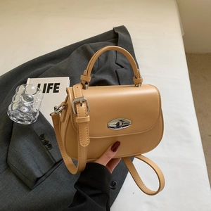 Chic beige crossbody saddle bag with silver buckle on elegant suit background