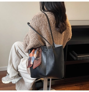 Détail d'un grand sac cabas noir mat avec un foulard en soie orange à motifs géométriques