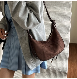 Gros plan d'un sac hobo en daim marron porté avec un manteau gris sur un escalier