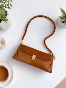 Detailed top view of a caramel brown baguette bag with gold buckle on white surface