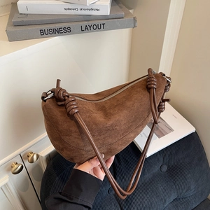 Brown suede crescent bag with knot detail and shoulder strap shown in aesthetic setting