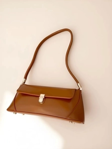 Detail view of caramel brown baguette bag with golden buckle and sleek leather texture