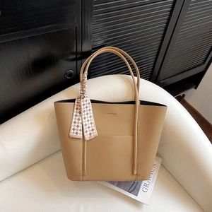 Light brown pebbled leather tote bag with elegant checkered scarf on white sofa
