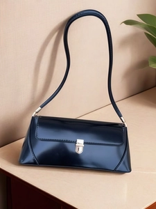 Detailed close-up of dark blue patent leather bag with golden shield buckle and slim strap