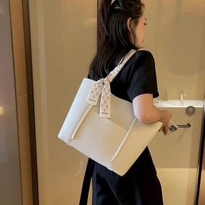 White faux leather tote bag with stylish silk scarf detail on a model in a warm interior