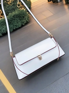 Close-up of white minimalist baguette bag with burgundy piping and gold metal buckle