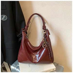 Detail of burgundy patent leather tote with knot handle and metallic charm on luggage