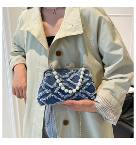 Detail of navy denim shell bag with frayed edges, pearl handle, and kiss-lock closure