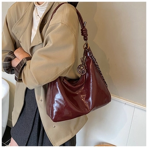 Detail of burgundy patent leather tote bag with braided knot strap and metal charm on shoulder