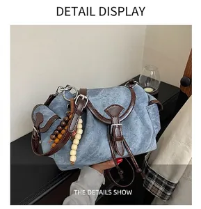 Detail view of denim shoulder bag featuring dark brown leather trim and beaded pendant