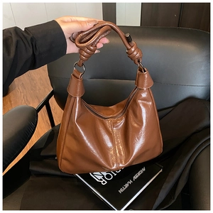 Detailed close-up of brown glossy tote bag with twisted handle and metal ring connector