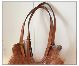 Detail of woven leather tote strap attached with silver rings on a brown shoulder bag