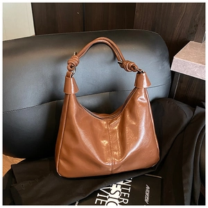 Detail of caramel brown glossy PU leather tote bag featuring a decorative knot on the strap