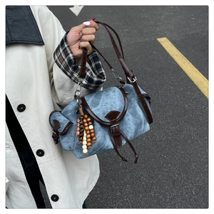Detail of blue textured denim bag with brown leather trim and wooden bead charm accessory
