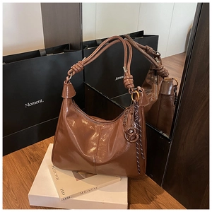 Detail of glossy brown leather tote bag showing rope knot handle and woven charm