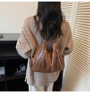 Detail view of brown leather bag with fringe zippers worn with a cozy knit sweater
