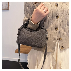 Detail of grey knitted cylinder crossbody bag featuring a ruched handle and metal hooks