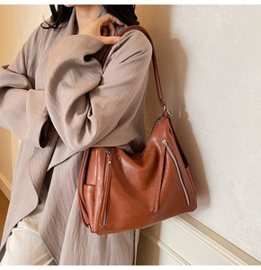 Detail of a brown leather shoulder bag with decorative dual zippers and side pocket