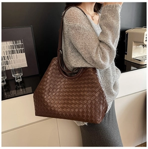 Detail of a large woven tote bag in dark brown leather worn by a model in a modern home setting