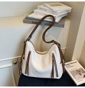 Detail of off-white hobo bag showing front zippers, brown straps and leather texture