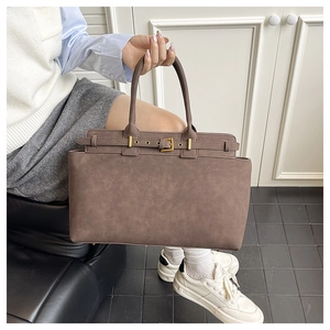 Detail of dark brown tote bag with suede texture and metallic buckle strap in a modern room