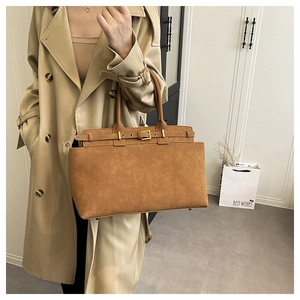 Close-up of brown suede handbag with belt buckle detail worn with a trench coat