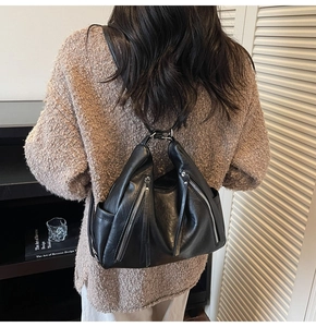 Detail of a black leather backpack with dual metal zippers worn over a brown knit sweater