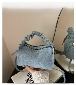 Detail view of stylish light blue denim handbag with ruched handle and dual zipper closure
