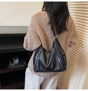Detail of a black hobo bag with silver zippers worn over a beige knit sweater