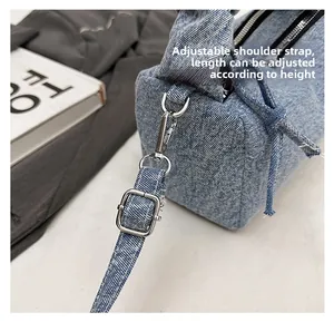 Detail view of denim shoulder bag featuring metal lobster clasps and adjustable buckle