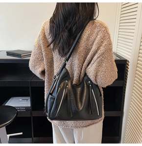 Detail of black leather hobo bag featuring dual vertical zippers and long fringe tassels