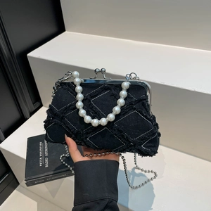 Retro black denim shell bag with pearl handle and metal chain in a minimalist setting