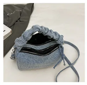 Detail view of denim shoulder bag featuring double zippers and pleated handle design