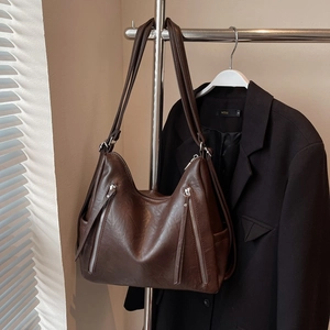 Detail view of large dark brown crossbody bag with side pockets and decorative zippers
