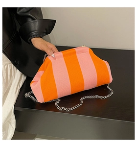 Détail d'une pochette en tricot rayée rose et orange avec chaîne argentée sur bois
