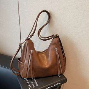 Close-up of brown textured leather handbag featuring long tassels and metal zippers