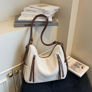Detail of a minimalist cream leather crossbody bag with brown straps and silver hardware
