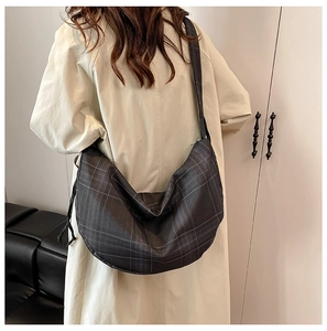 Detail of grey plaid crossbody bag with drawstring texture on a model wearing a trench coat