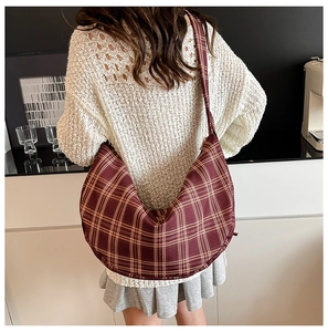 Detail of red-brown plaid hobo cross-body bag with wide strap worn by a model