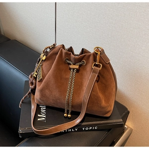 Detail of a brown suede drawstring bucket bag with leather trim on a magazine