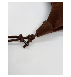 Detailed macro of brown suede shoulder bag featuring a knotted strap and silver metal tubes