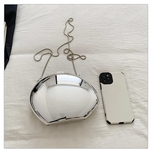 Close-up of silver mirror acrylic evening bag with metal chain on white fabric background