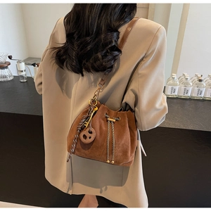 Detail view of brown suede bucket bag with vintage charms on a beige blazer outfit