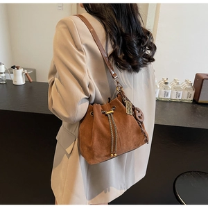 Detail of brown suede bucket bag with drawstring closure and vintage metal charms