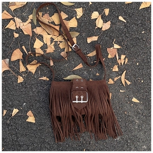Gros plan du sac à bandoulière marron à franges avec boucle argentée sur feuilles