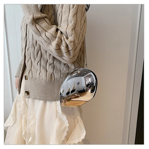 Silver mirror pebble clutch bag with metal chain shown on model in khaki knit cardigan
